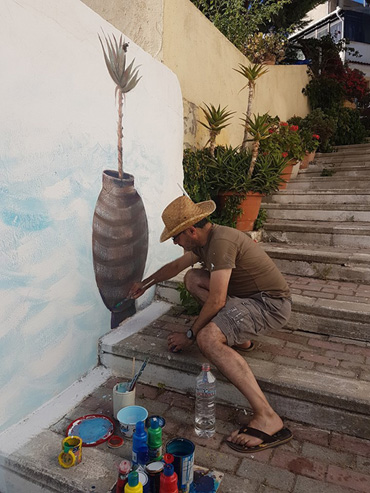 Thumbnail image of George Sfougaras painting a mural in Potamies - Art Abroad - George Sfougaras Paints In Potamies